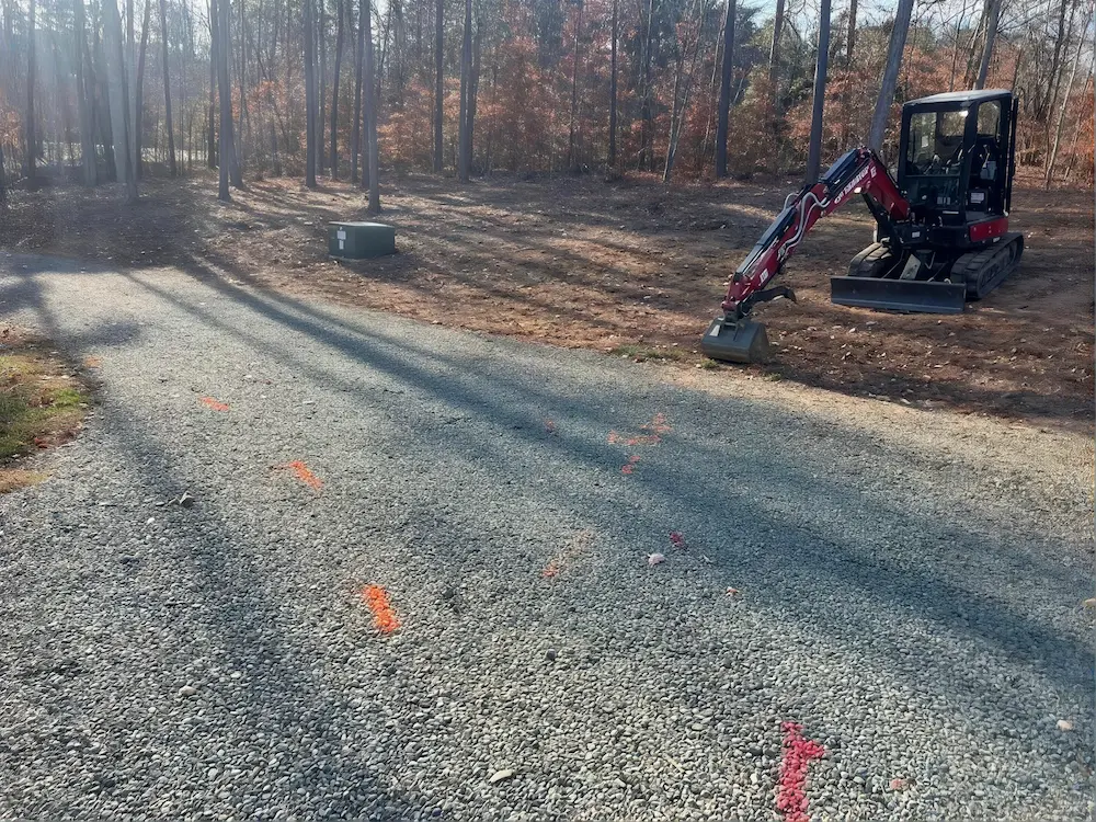 Mini excavator shaping a new gravel driveway through the woods.