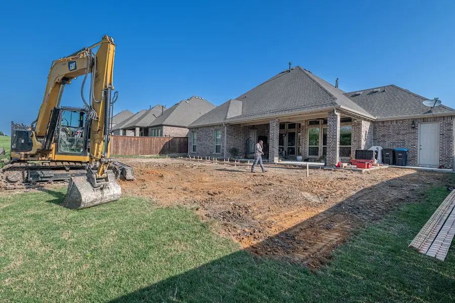 Graded and staked yard ready for site work beside a finished house.